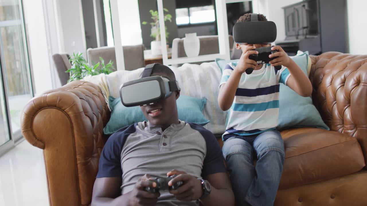video de un feliz padre e hijo afroamericanos sentados en el sofá y jugando juegos con auriculares vr