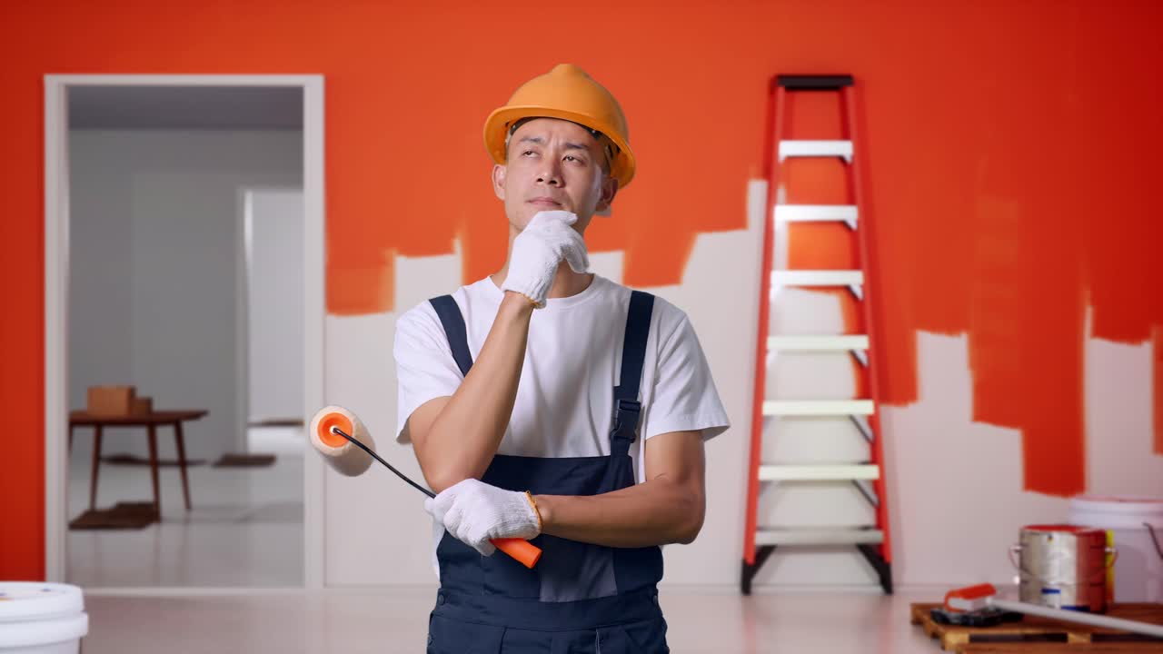 Asian Man Painter Wearing Safety Helmet Thinking And Looking Around Then Raising His Index Finger While Standing With Painting Wall In Room