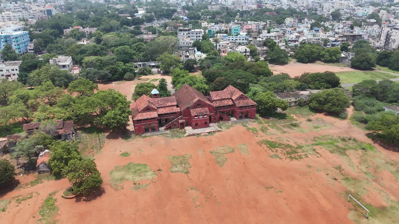 Wide-angle aerial footage of a peaceful building through open green spaces with buildings in background.