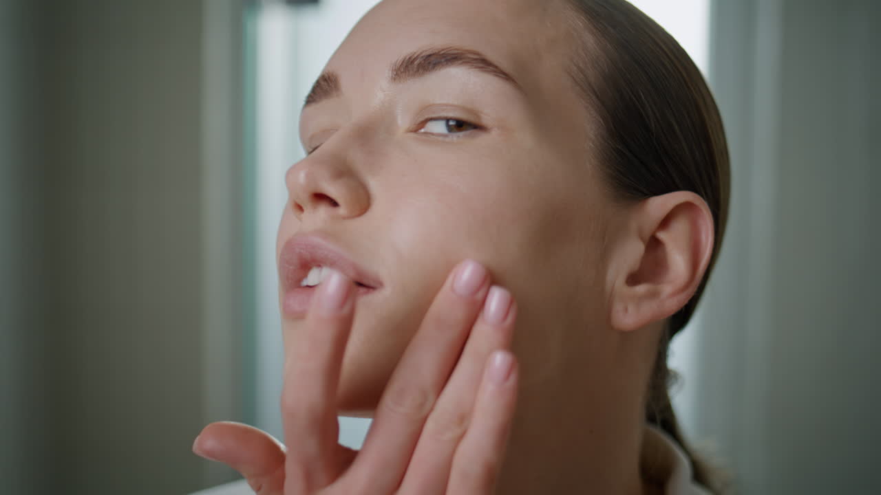 Lady massaging face lotion in bathroom closeup. Serene woman looking camera