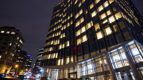 low angle view of a modern office building at night, with lights on in many windows and a red logo displayed on the facade, suggesting ongoing activity