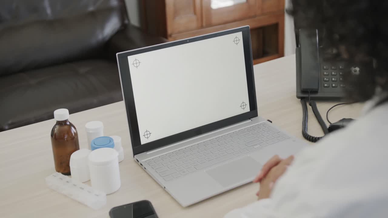 doctora biracial sentada en un escritorio y usando una computadora portátil con espacio para copiar, cámara lenta