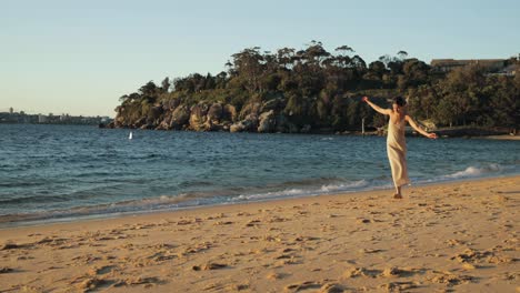 plano amplio de una joven mediterránea camina por la playa con un vestido largo durante una hermosa puesta de sol