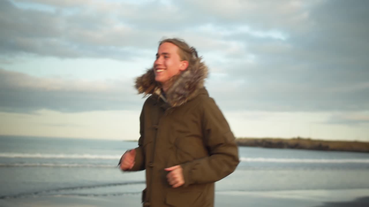 Young blond cheerful man is running along the beach