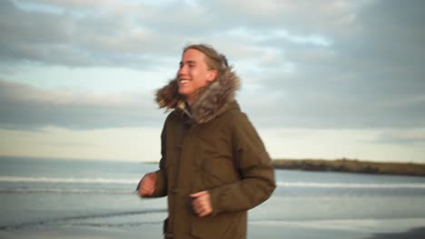 Young-blond-cheerful-man-is-running-along-the-beach