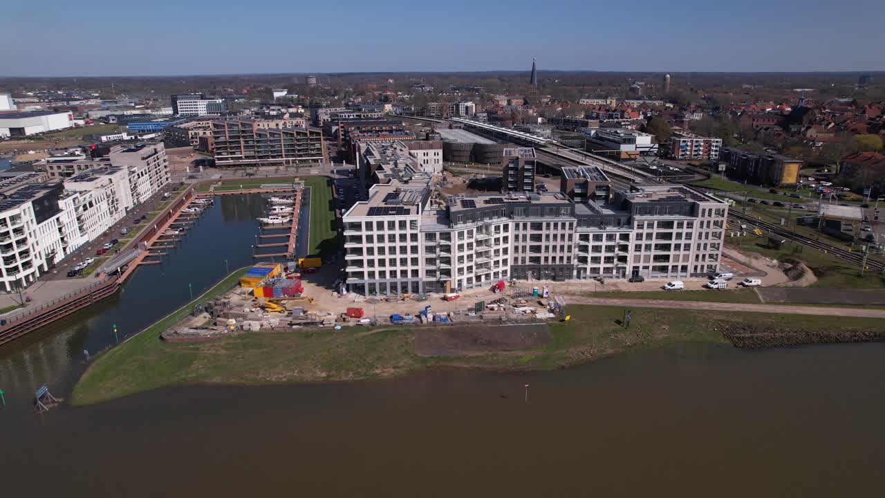 Panoramische luchtfoto van de bouw van het luxe appartementencomplex Kade Zuid aan de oever van de rivier de IJssel, tussen spoorlijnen en een recreatiehaven.