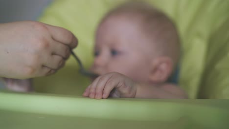 mommy gives meal to little son sitting in highchair at home