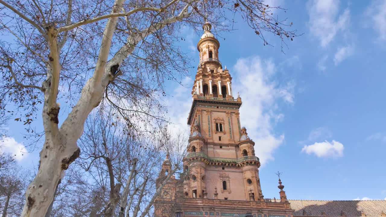 Historic brick tower with bare trees against blue sky at Plaza de España Seville Spain