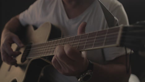 man playing and performing on an acoustic guitar with black background and soft warm light