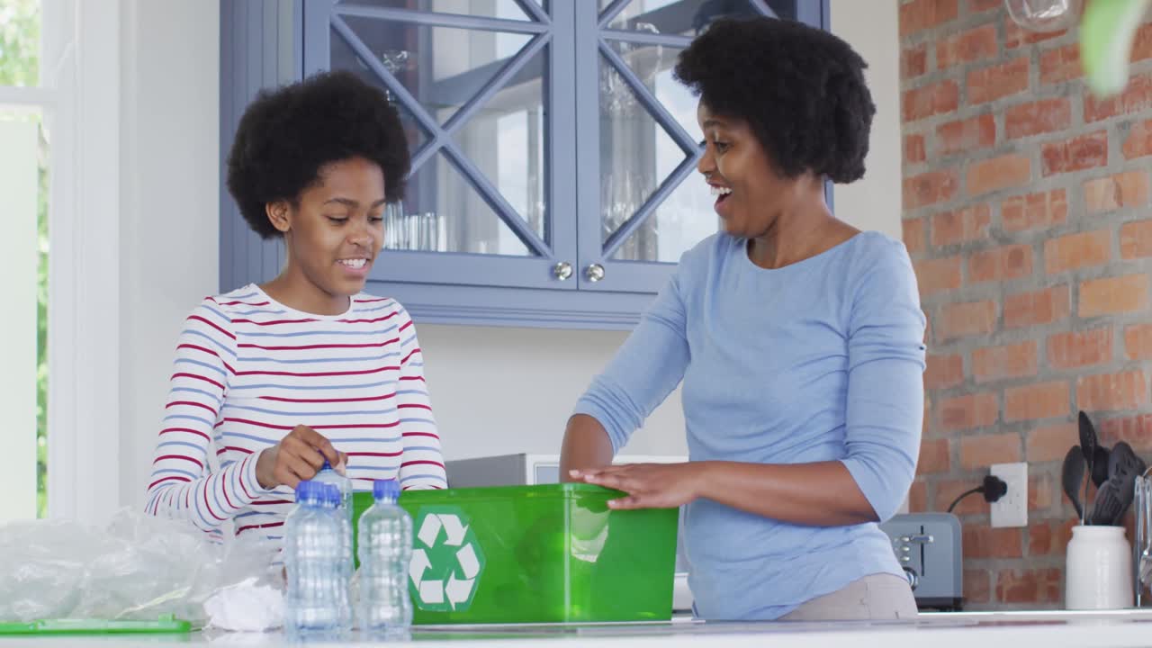 Happy african american mother and daughter recycling together in kitchen