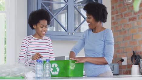 Happy-african-american-mother-and-daughter-recycling-together-in-kitchen