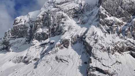 aerial-view-of-the-rugged,-snow-covered-cliffs-of-Fronalpstock-under-a-partly-cloudy-sky-in-Glarus-Nord,-Switzerland