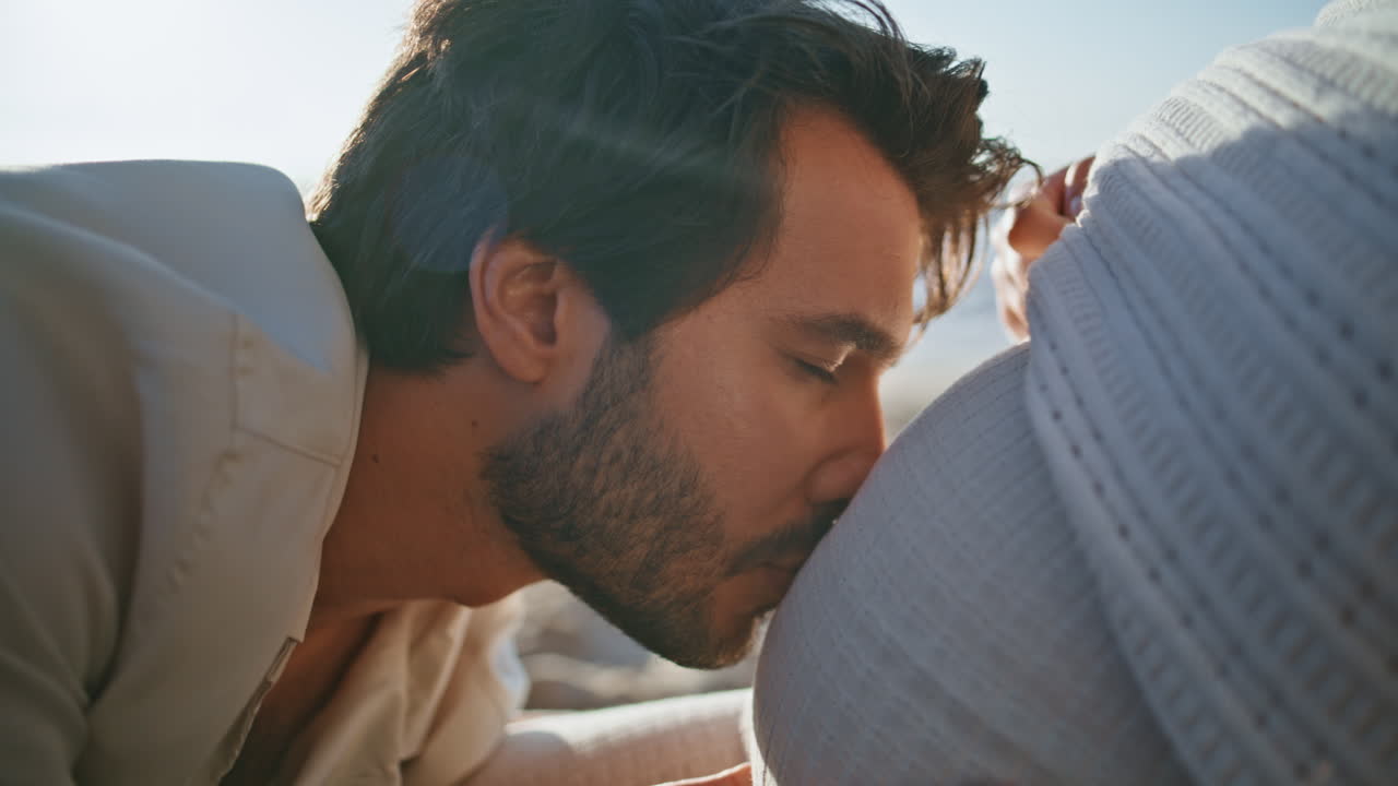 행복한 남자가 배를 키스하고 임신한 아내가 자연을 가까이 앉아 임신을 즐기고 있습니다.