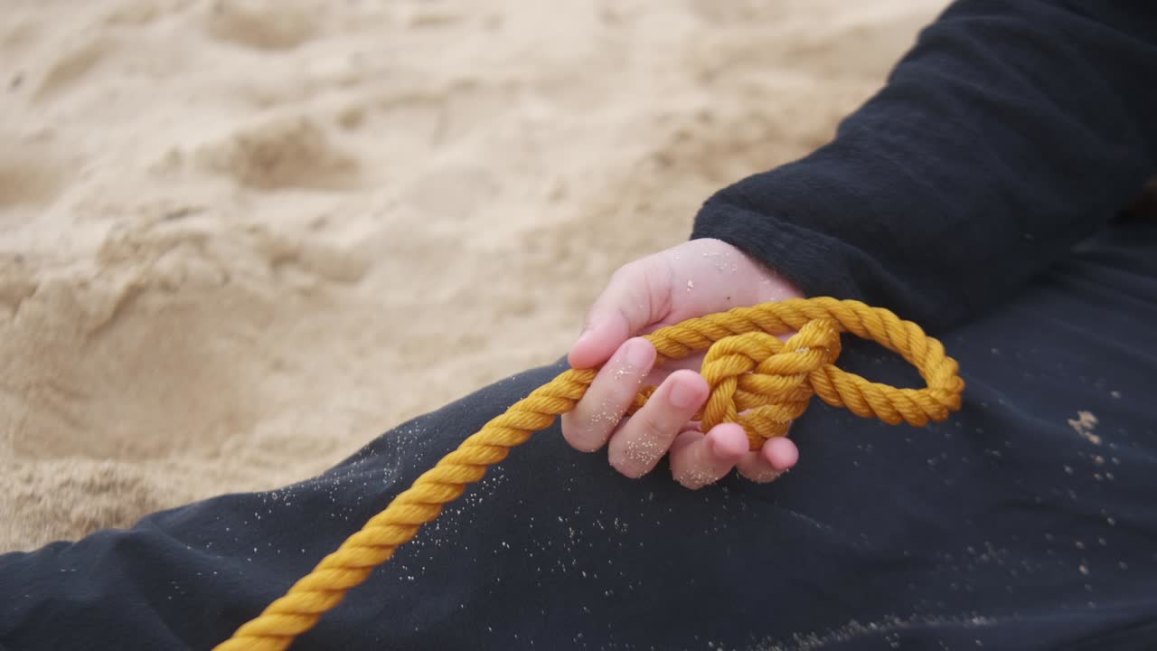 Hands Of Depressed Person Sitting On Sand, Holding Rope With Suicidal Thoughts. closeup shot