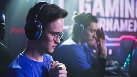 nerdy gamer preparing for video game match esportsman gamer in glasses putting on headphones and bumping fists with teammates at start of professional gaming tournament