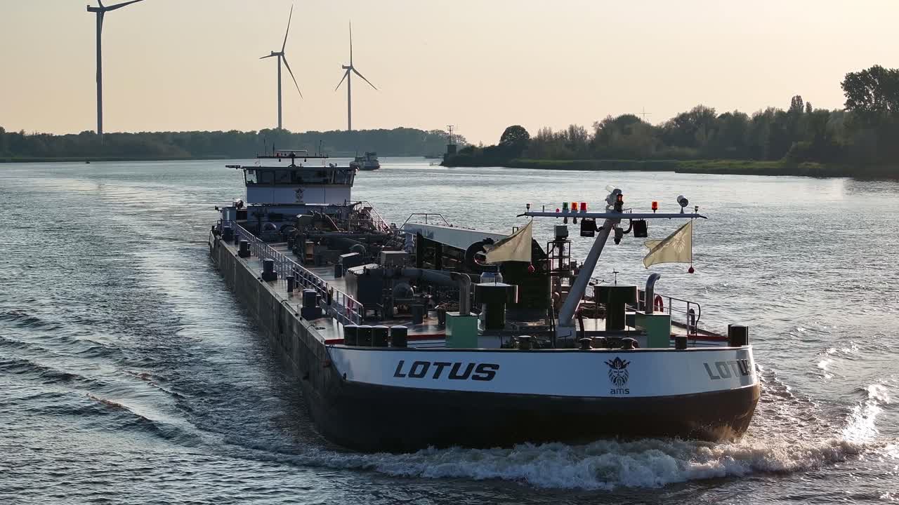 Dutch tanker ship Lotus on river with wind turbines in background, aerial pan