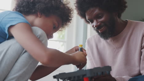 mixed race pre teen boy sitting on the floor with his father assembling a kit toy using a screw driver, close up, low angle