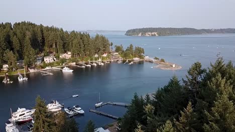 Aerial-View-Of-Sailboats-And-Yachts-Docked-At-The-Entrance-Of-Gig-Harbor-Marina-In-Gig-Harbor,-Washington-With-Motorboats-Speeding-On-The-Blue-Water---drone-shot,-slow-motion