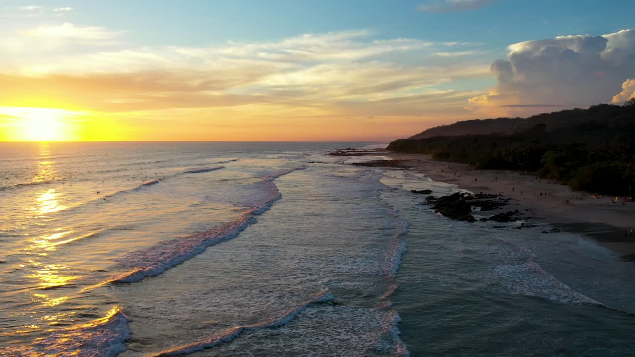 vuelo aéreo desde la playa hasta el atardecer reflejándose en el agua con olas y surfistas en el océano pacífico en tamarindo, costa rica
