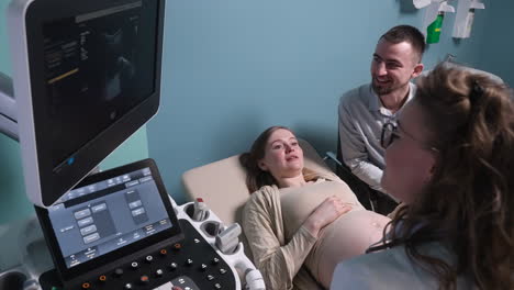 pregnant woman having ultrasound scan at the gynecologist office while loving husband holding her hand 12