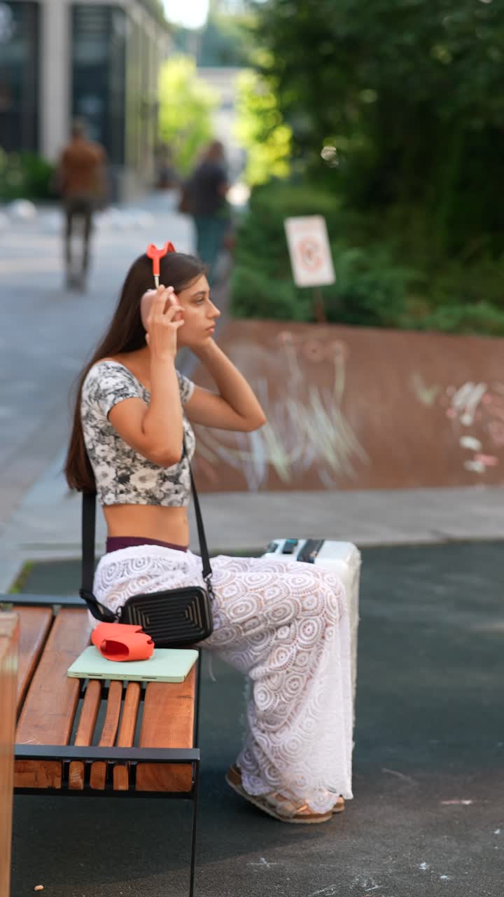 여성은 벤치에 헤드폰을 들고 야외에 있습니다.