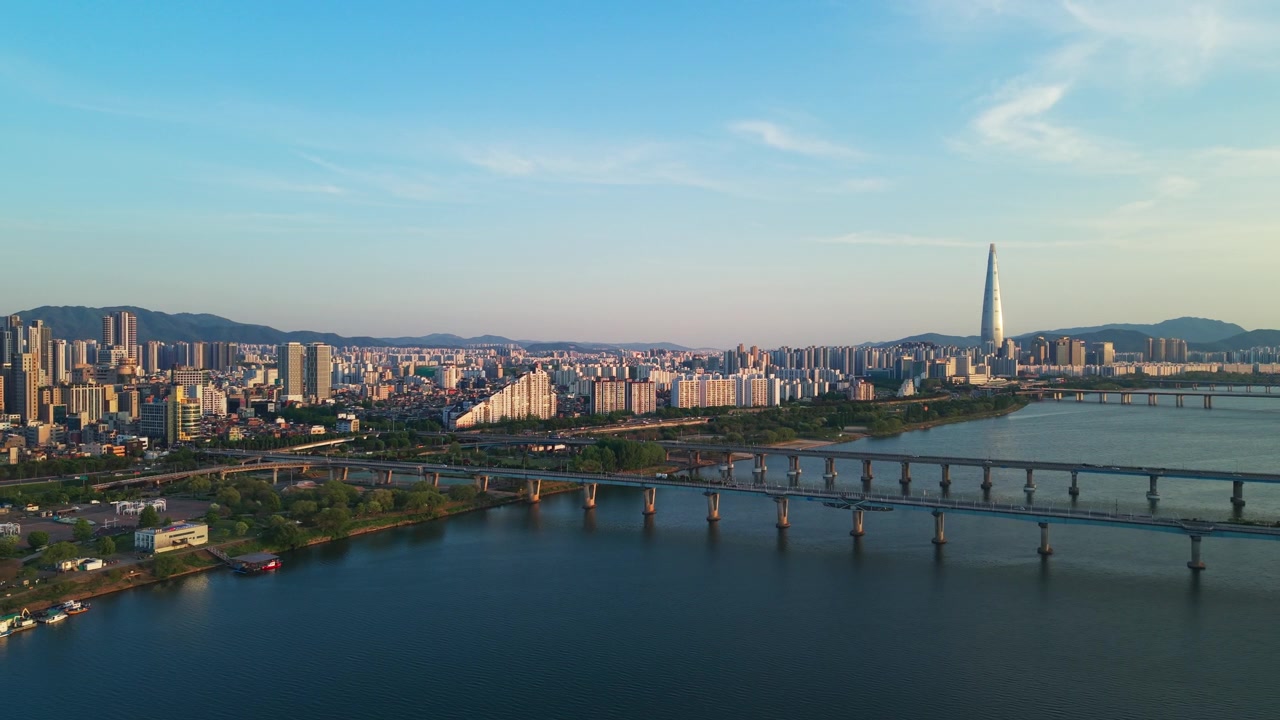Una ripresa aerea in allontanamento sopra il Parco Gwangnaru Hangang rivela il Ponte Gwangjin e il Ponte Cheonho che attraversano il fiume Han, con la Lotte World Tower nello skyline diurno primaverile di Seul, Corea.