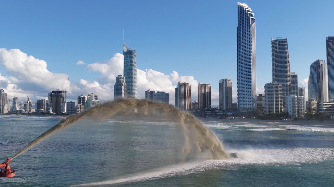 A dredging vessel pumps sand in front of Gold Coast skyscrapers under clear skies, highlighting coastal erosion management
