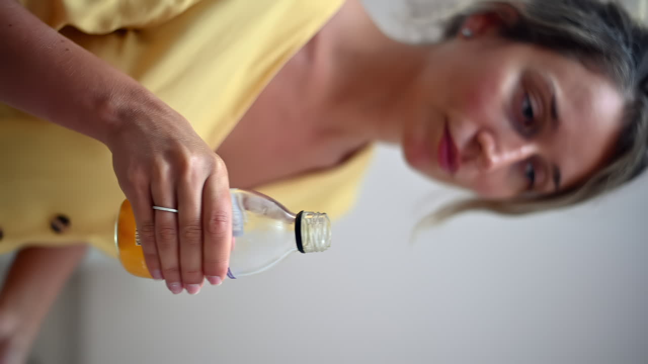 A woman in a yellow top skillfully opens a bottle to prepare a refreshing drink. The home setting creates a casual and enjoyable atmosphere for her activity