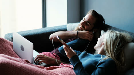 couple listening music on mobile phone while using laptop in living room 4k