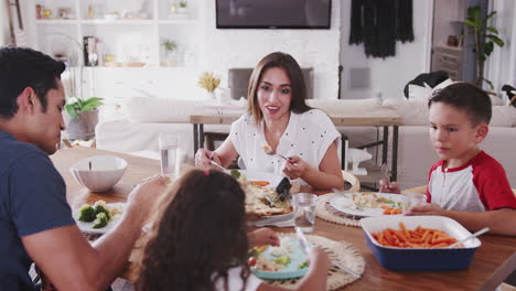 una joven familia hispana sentada en la mesa de comedor en casa cenando juntos