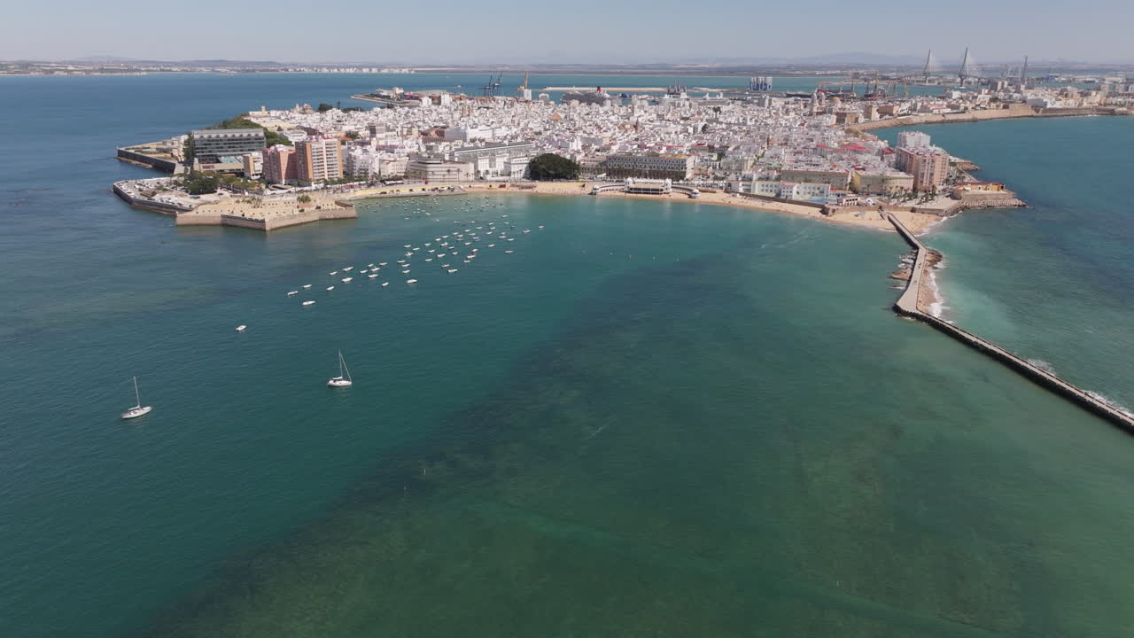 Veduta aerea in drone del paesaggio urbano di Cadice, in Spagna, Andalusia, Europa, in una luminosa giornata di sole, con vista sull'iconica e famosa spiaggia de La Caleta e sul lungomare della città. Drone in volo in avanti