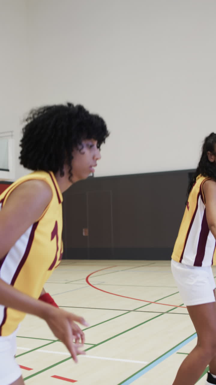 Vertikal video af mangfoldigt kvindeligt basketballhold, der træner på indendørs bane, i slowmotion