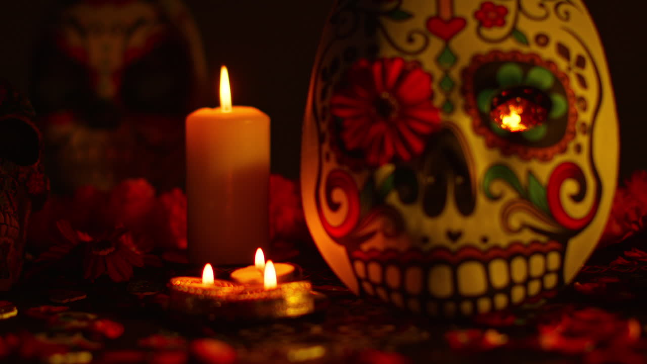 close up de máscaras y cráneos decorados rodeados de velas y pétalos de flores celebrando la fiesta mexicana de dia de muertos o día de los muertos contra un fondo oscuro