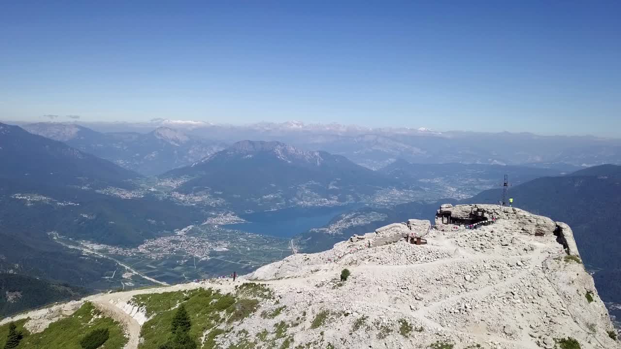 Luftfoto af en ung mand, der står på toppen af Cima Vezzena, Pizzo di Levico, med drone, der flyver fremad med panoramaudsigt over Trento, Italien.