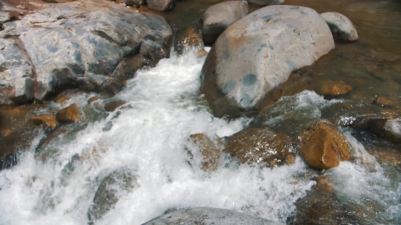 toma en cámara lenta de agua que fluye a través de rocas de guijarros en un río claro