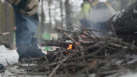 man placing twigs on small fire in a camp ground