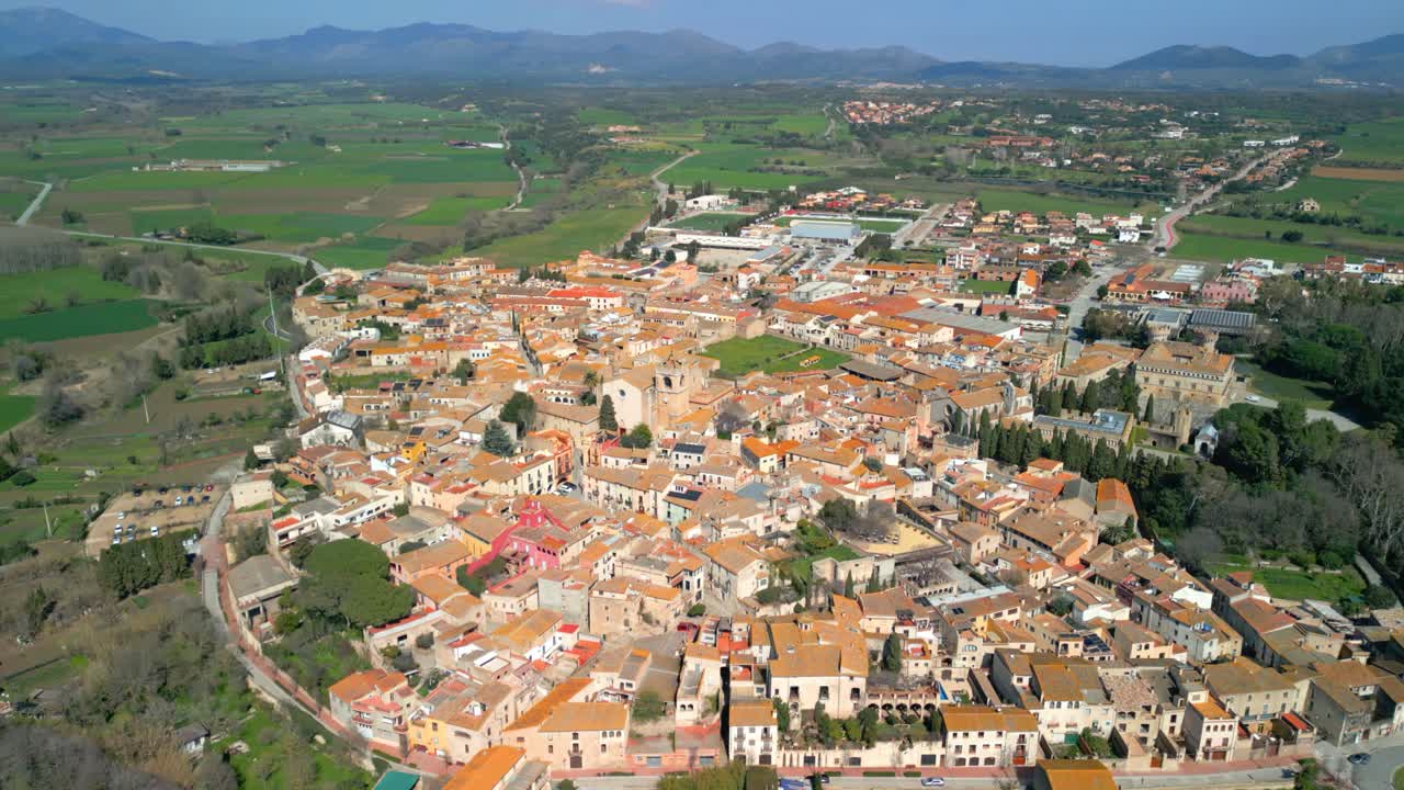 Peralada peralada, a charming town in catalonia, showcases its traditional architecture with terracotta rooftops, surrounded by a verdant landscape and distant mountains under a clear blue sky