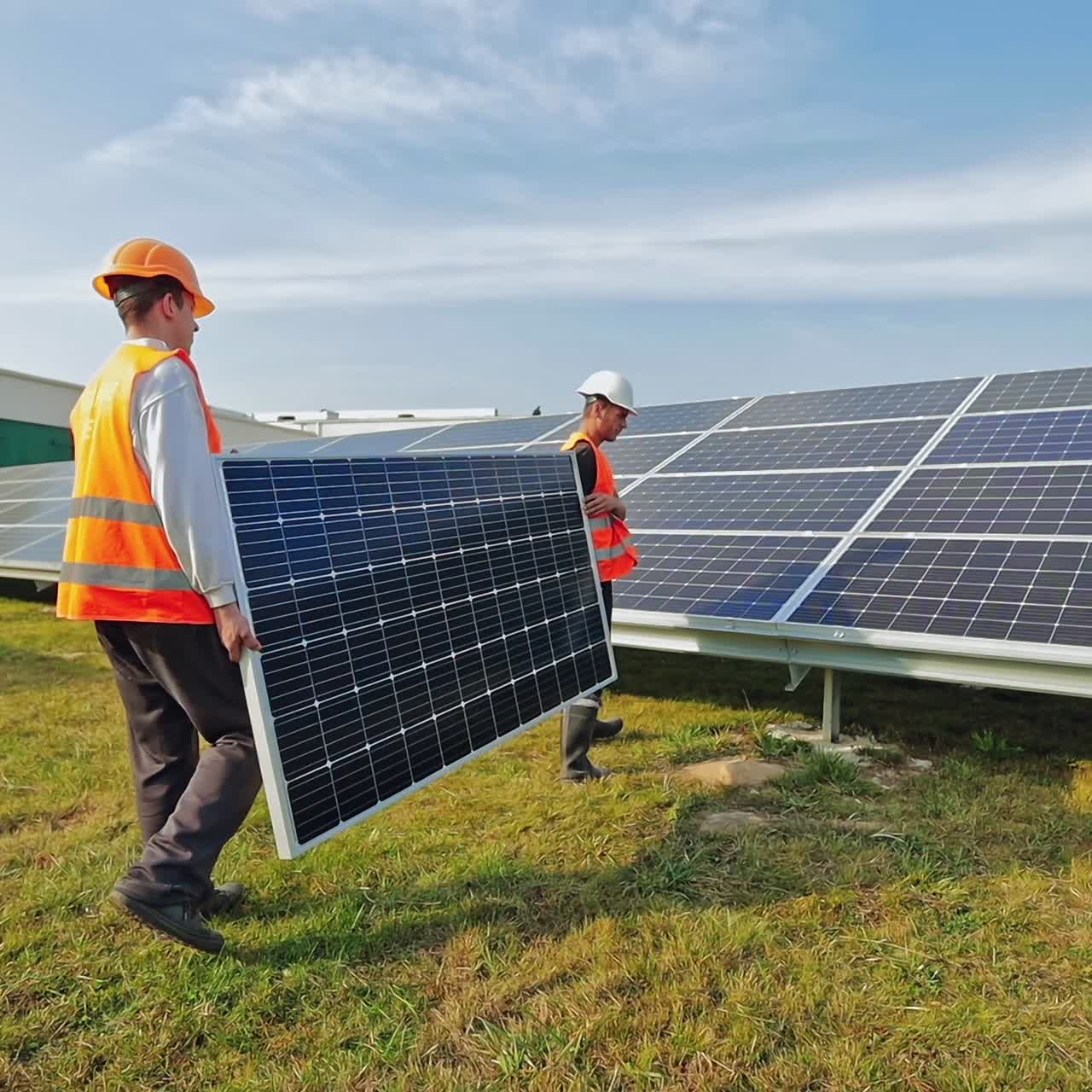 Installing photovoltaic battery. Workers with new solar panel in a sunny day. Two technicians in protective uniform with hard hats carrying sunny battery.