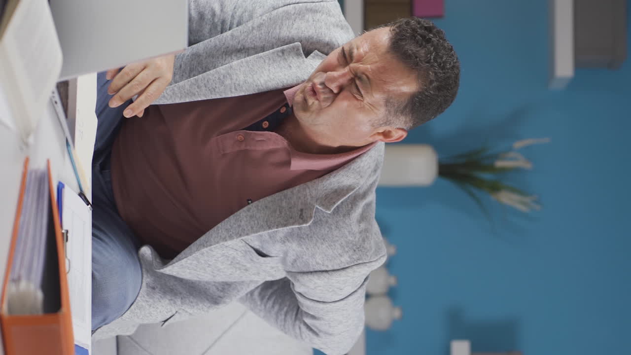 vídeo vertical de un trabajador de oficina en casa un anciano tiene dolor de espalda.