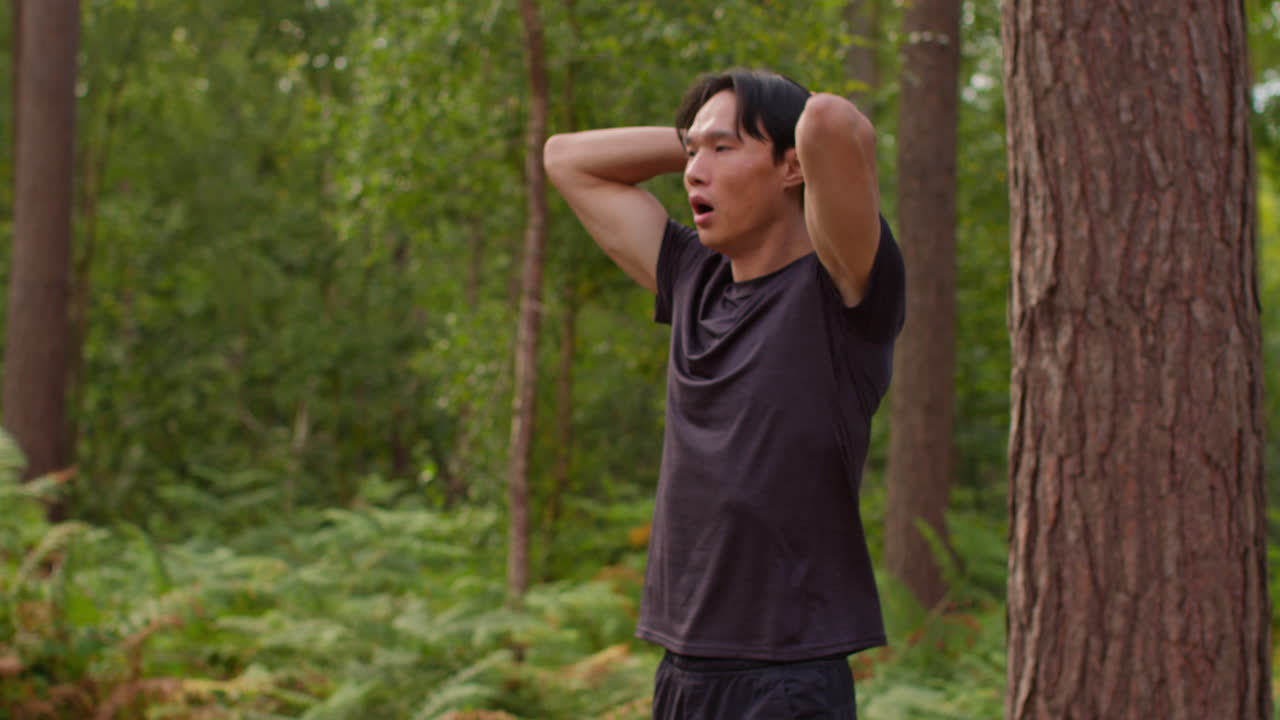 피곤한 중성인 남자가 야외에서 운동을 하고 숲 속의 트랙을 따라 달리며 숨을 쉬고 활동 앱을 확인하고 스마트 시계에서 실시간으로 찍은 사진입니다.