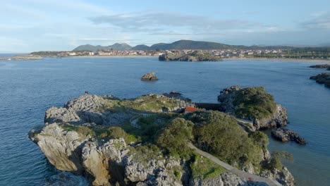 tomada orbital aérea de una pequeña península por el cabo quejo con una pequeña casa y una piscina natural, costa cantábrica