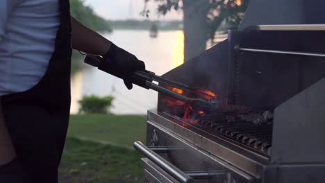 close up of griller barbecue grill party at sunset garden lake mexican latin service cooker flames on grid and turning steak meat raw