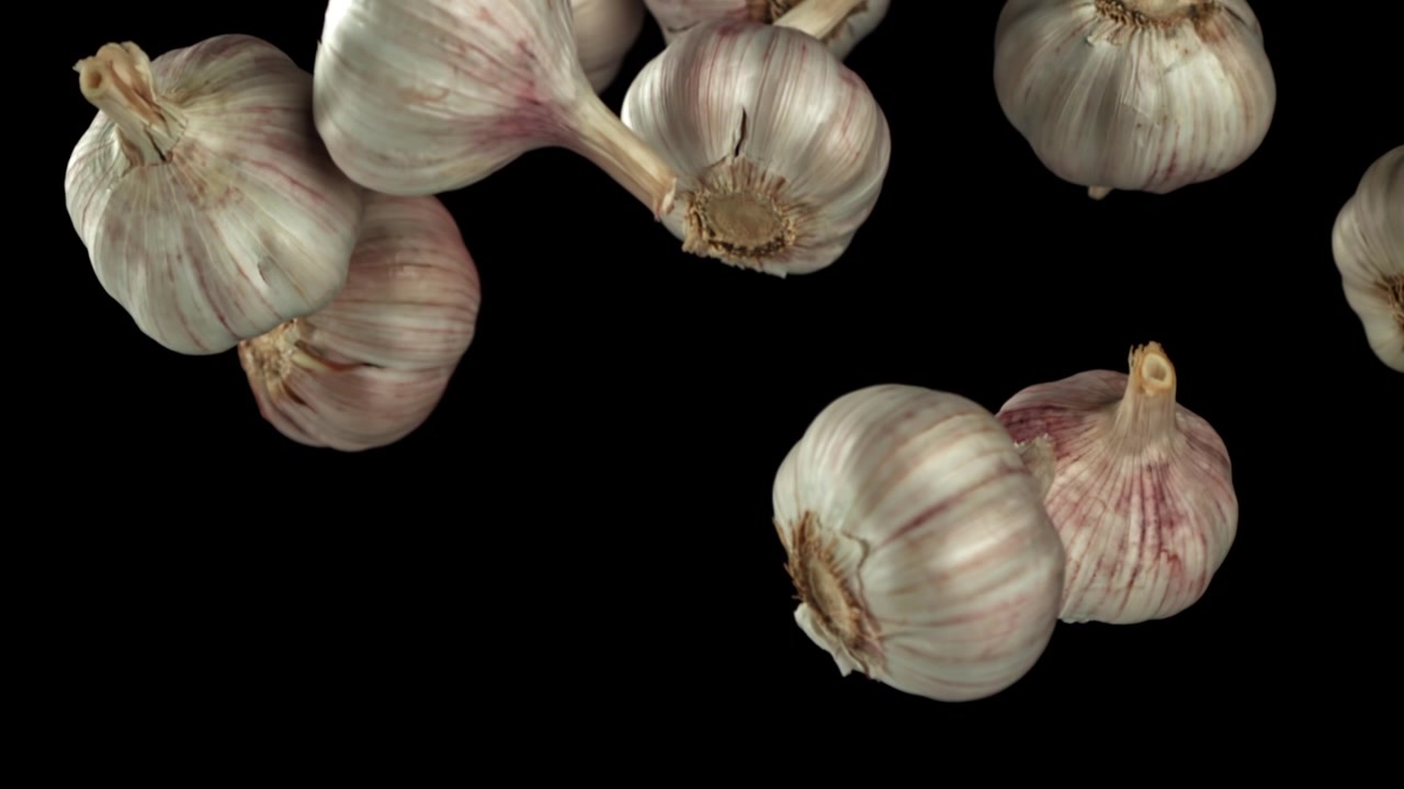 Teste d'aglio fresche che cadono e galleggiano su uno sfondo nero