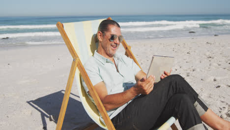 älterer kaukasischer mann sitzt auf sonnenliegen am strand.