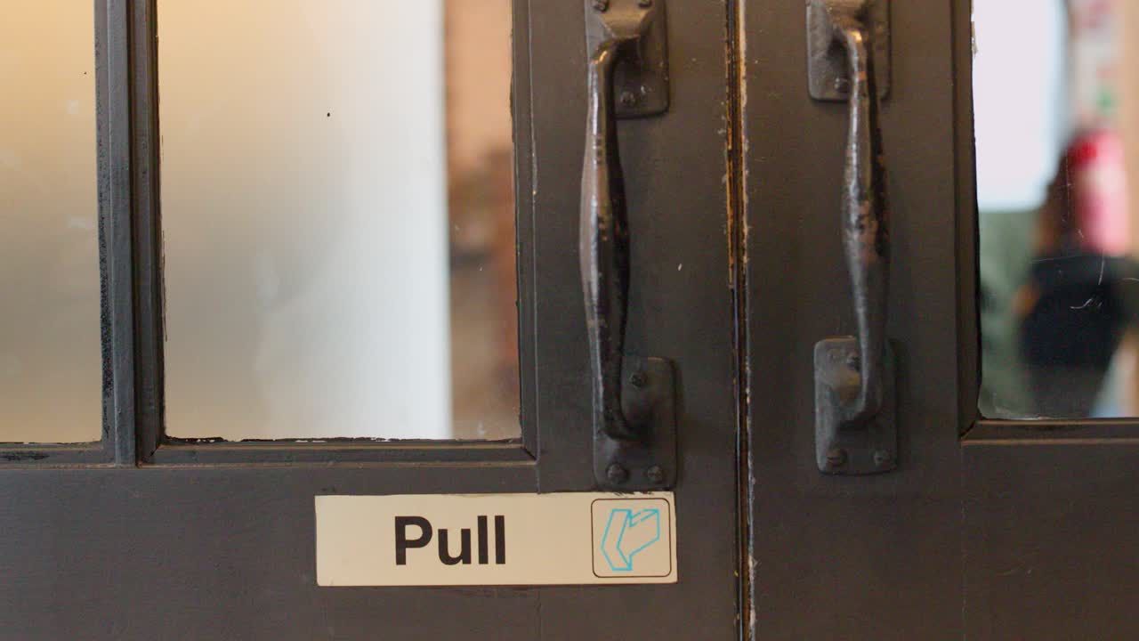 Man in casual clothing opens labeled door, entering warmly lit interior, camera follows from behind