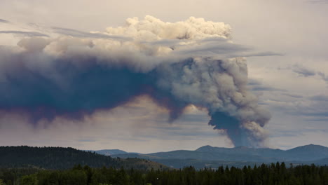 large smoke plume from a wildfire over a mountainous forest