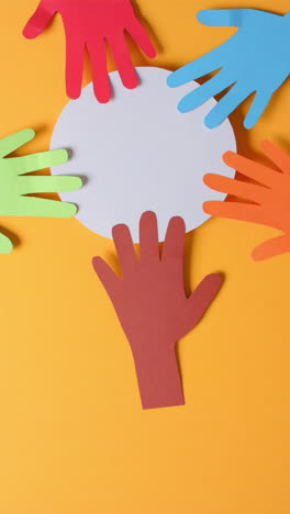 vertical video of hands touching circle made of colourful paper on orange background with copy space