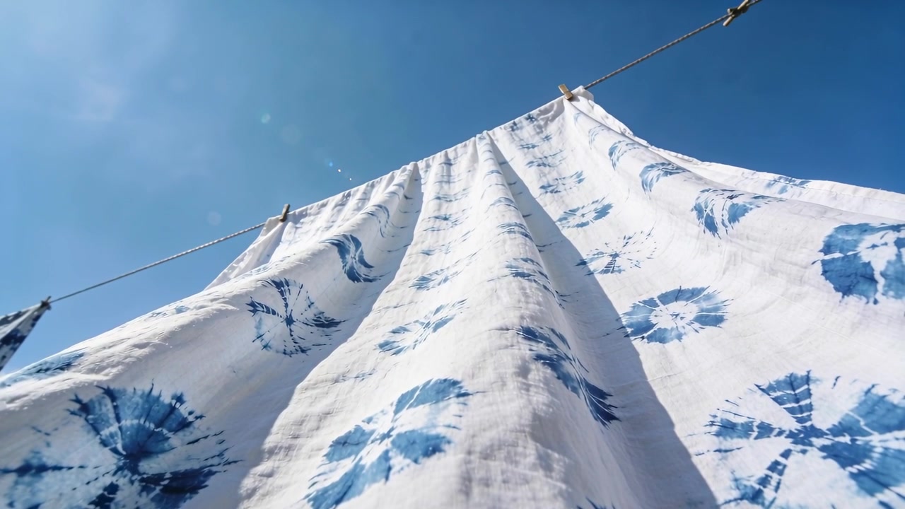 Light breeze causing large white tie-dye sheet billowing on rope in yard, clothespins, lens flare