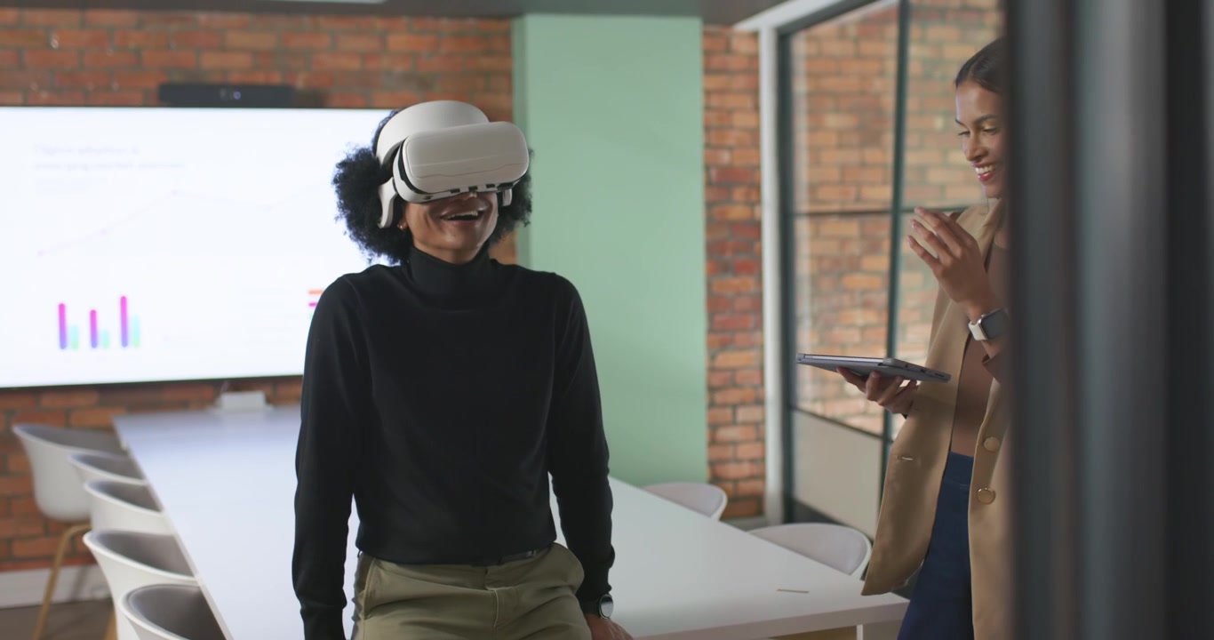 Coppia afroamericana che dimostra un visore VR in ufficio, con la donna che usa un tablet e l'uomo in dolcevita che reagisce