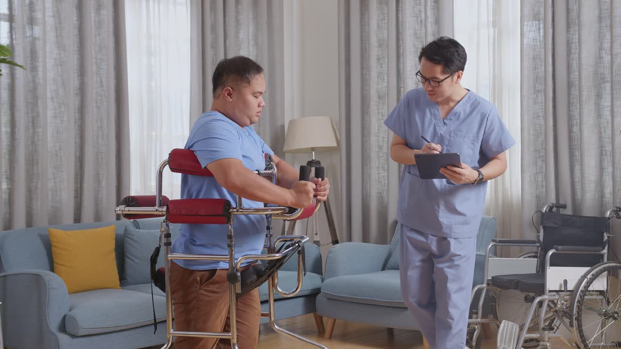 아시안 남성 간호사가 커를 사용하는 환자에게 손을 흔들며 집에서 물리 치료를하는 동안 태블릿에서 보고 녹음하는 측면 뷰